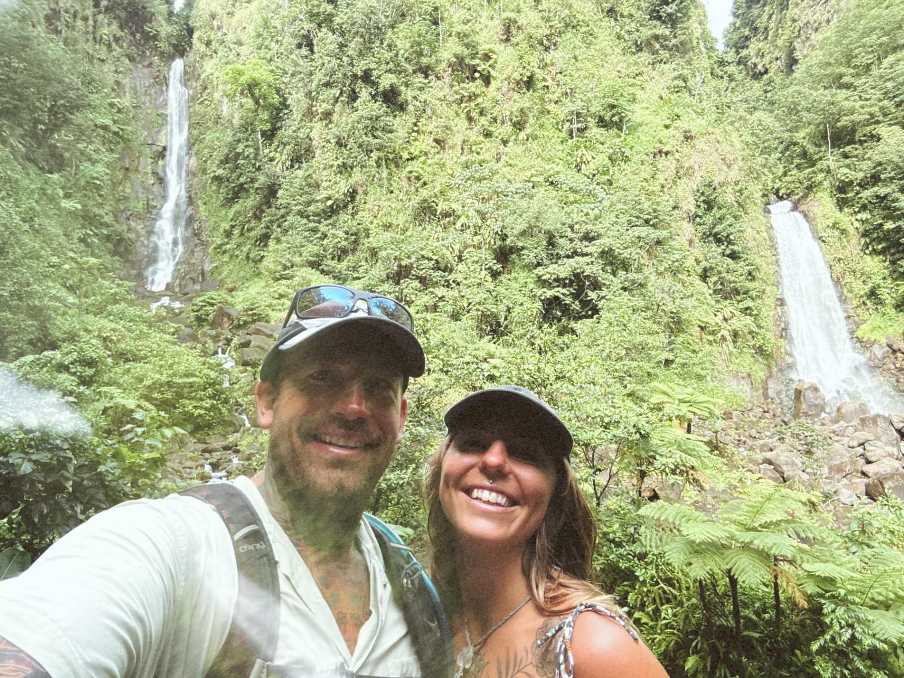 Gina and Cody smiling on a rainforest hike between twin waterfalls