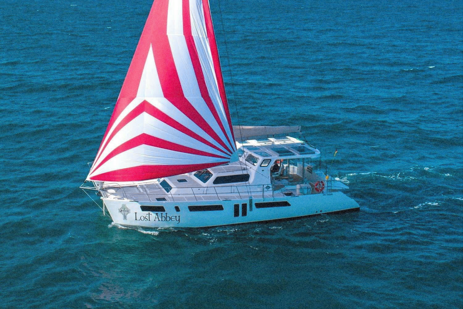 Lost Abbey sailing under a red and white striped spinnaker on bright blue water
