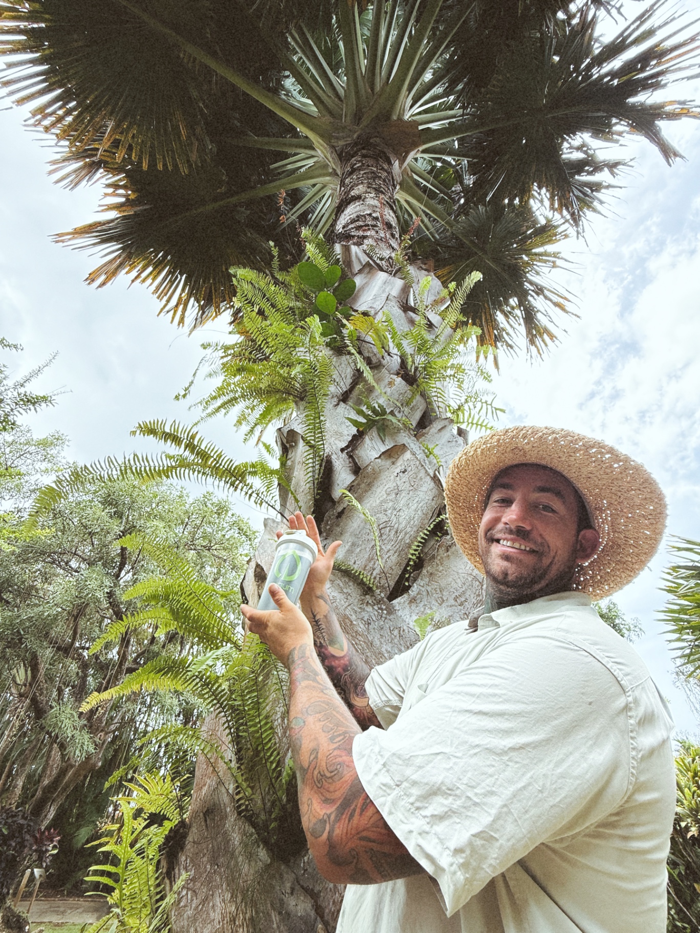Cody in a straw hat beside a tall palm tree