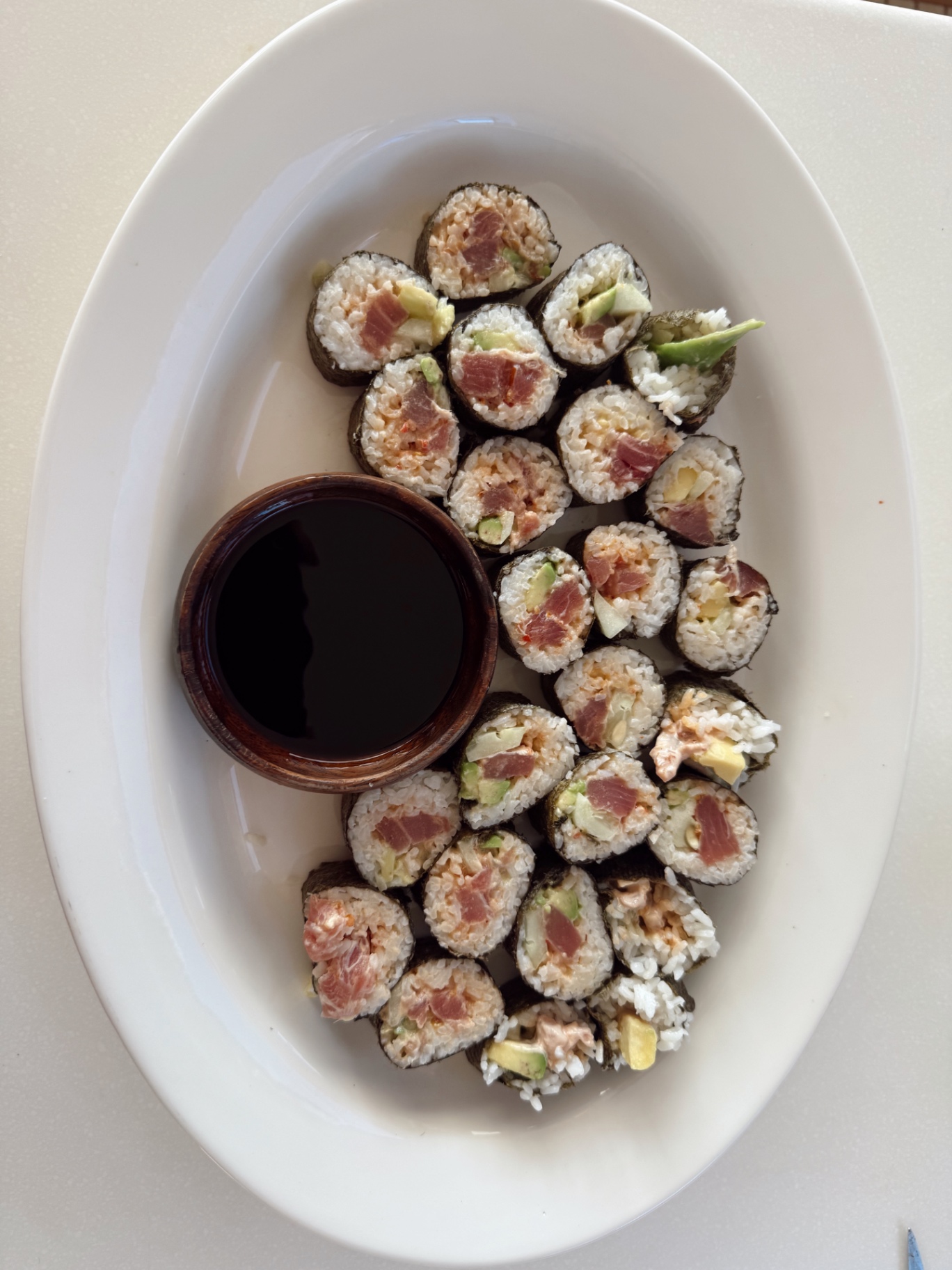 A platter of homemade tuna sushi rolls with a small bowl of soy sauce
