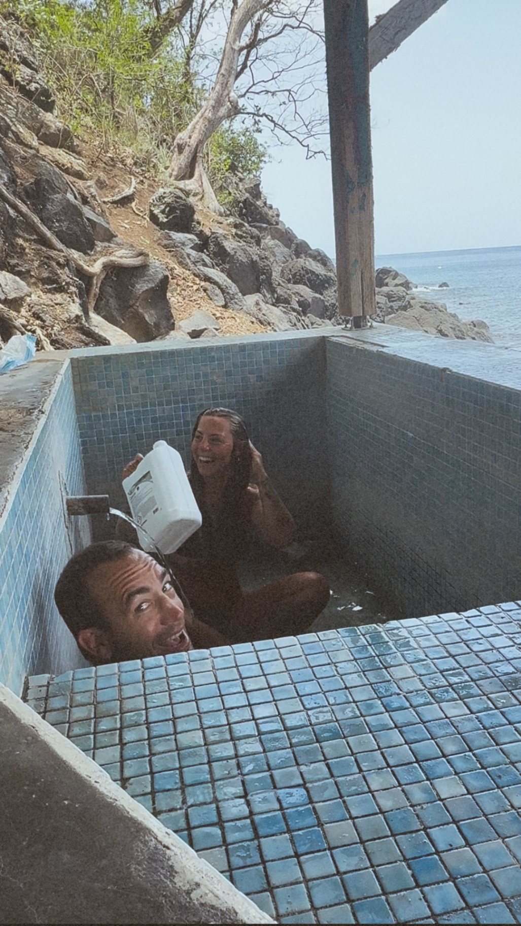 Gina and Cody laughing together in a seaside hot spring above the ocean