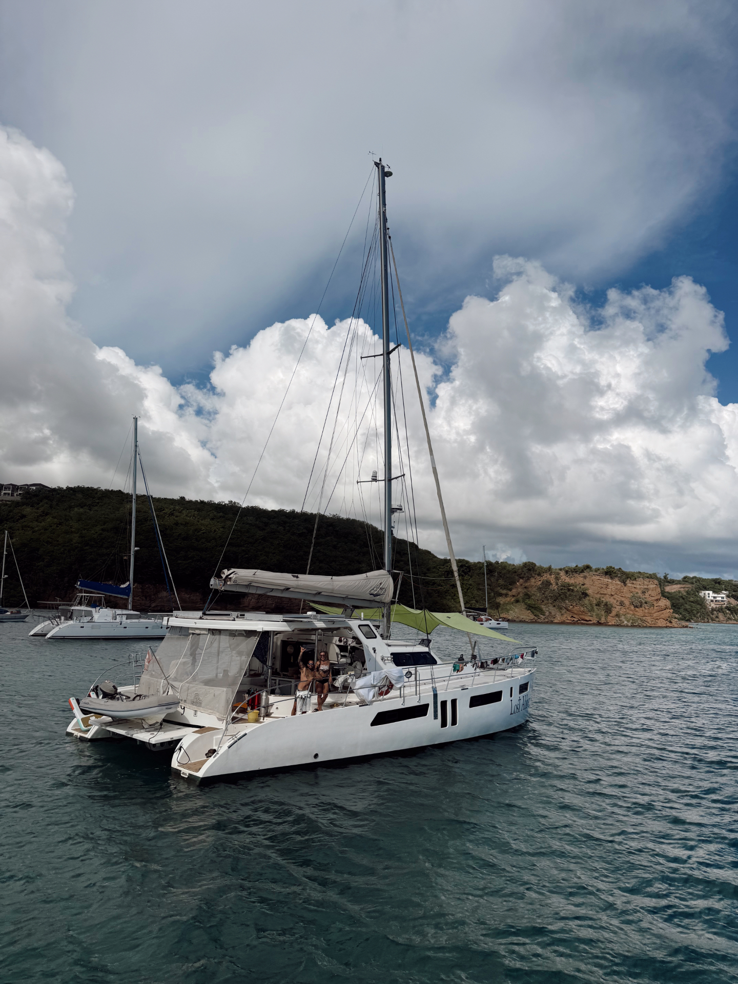 Lost Abbey anchored in a bay with lush green hills behind her under a dramatic cloudy sky